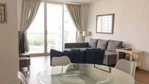 A living room with a glass table, two sofas, a TV, and a window with curtains. - Komffy Apt w/2 Queen Beds and Canal View at Tides (Hollywood)