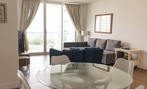 A living room with a glass table, two sofas, a TV, and a window with curtains. - Komffy Apt w/2 Queen Beds and Canal View at Tides (Hollywood)