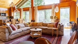 Un accogliente interno di una baita con un grande tavolo da pranzo in legno, un divano e un angolo cottura.