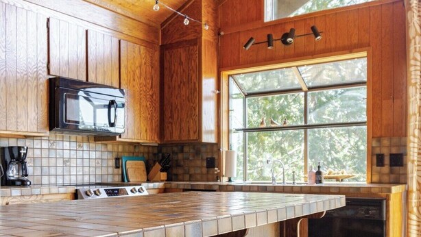 Una cucina moderna con mobili in legno, un'isola grande con sgabelli, un forno a microonde e una finestra con vista sugli alberi.