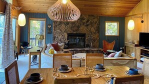 Un accogliente interno di una baita con camino in pietra, soffitto in legno e zona pranzo con tavolo apparecchiato per due.