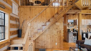 Un interno in legno con una scala, un angolo cottura e un soggiorno con un divano marrone.