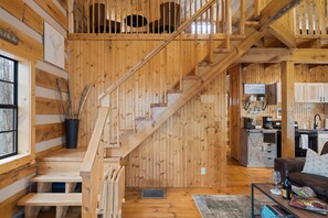 A wooden interior with a staircase, a kitchen area, and a living room with a brown sofa.