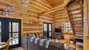 Interno di una baita di legno con un divano, un tavolo da pranzo e un televisore.