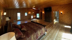 Een ruime slaapkamer met een groot bed, houten plafond en een aan de muur bevestigde televisie.