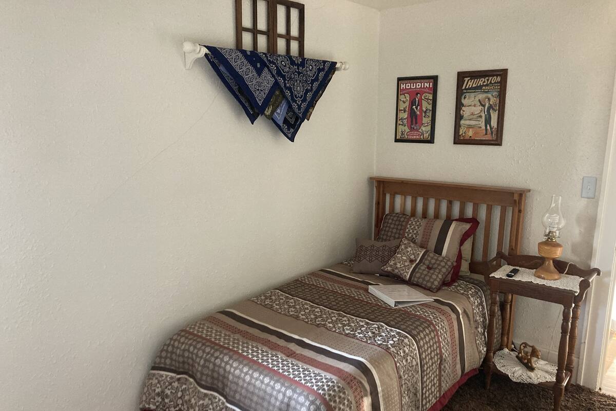 A bedroom with a wooden bed, patterned bedding, a bedside table with a lamp, and two posters on the wall.
