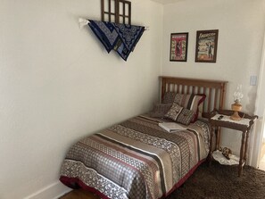 A bedroom with a wooden bed, patterned bedding, a bedside table with a lamp, and two posters on the wall. - The Coffey House (Choteau)