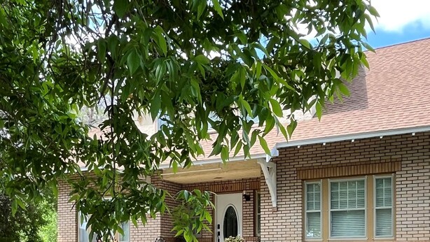 A two-story house with a brick exterior, a front porch, and a small garden area. - The Coffey House (Choteau)