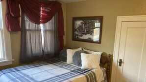 A bedroom with a bed, a painting on the wall, and a door. - The Coffey House (Choteau)