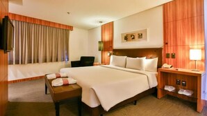 A hotel room with a large bed, a bedside table with a lamp, a chair, and a wooden wardrobe.