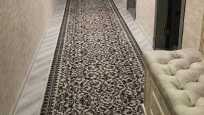 A narrow hallway with patterned carpet, light-colored brick walls, and a tufted sofa on the right. - King sized bed,luxury house (Тошкент)