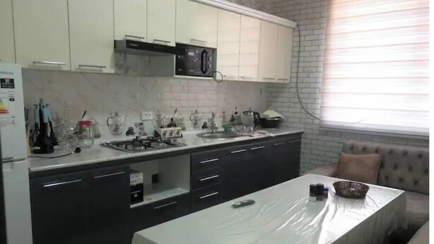 A kitchen with a microwave, stove, and sink. There is a couch and a window with blinds. - King sized bed,luxury house (Тошкент)