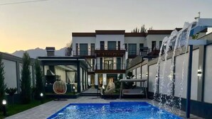 A modern hotel with a swimming pool, outdoor seating, and a view of mountains in the background. - Best place for vacation (Тошкент)