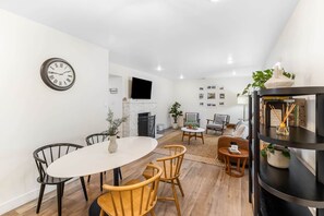 Ein modernes Wohnzimmer mit Kamin, einem Essbereich mit rundem Tisch und Stühlen sowie einem an der Wand befestigten Fernseher.