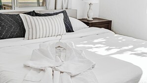 Ein ordentlich bezogenes Bett mit weißer Bettwäsche, einem gestreiften Kopfkissen und einem weißen Bademantel.
