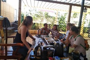 A group of people around a table with various items, including a kettle and containers, in an outdoor setting with a wooden structure overhead. - Kevin Boutique Hotel (Guilin)