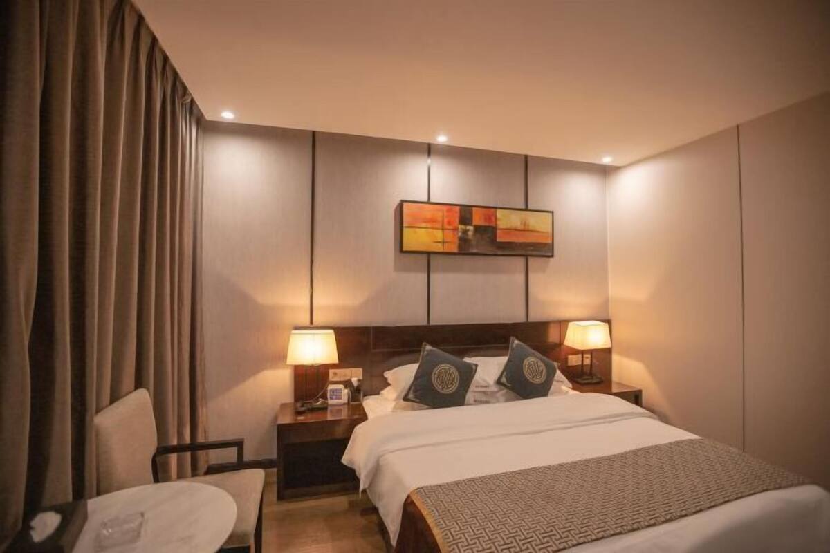 A hotel room with a bed, two bedside tables with lamps, a chair, and a wall-mounted artwork.