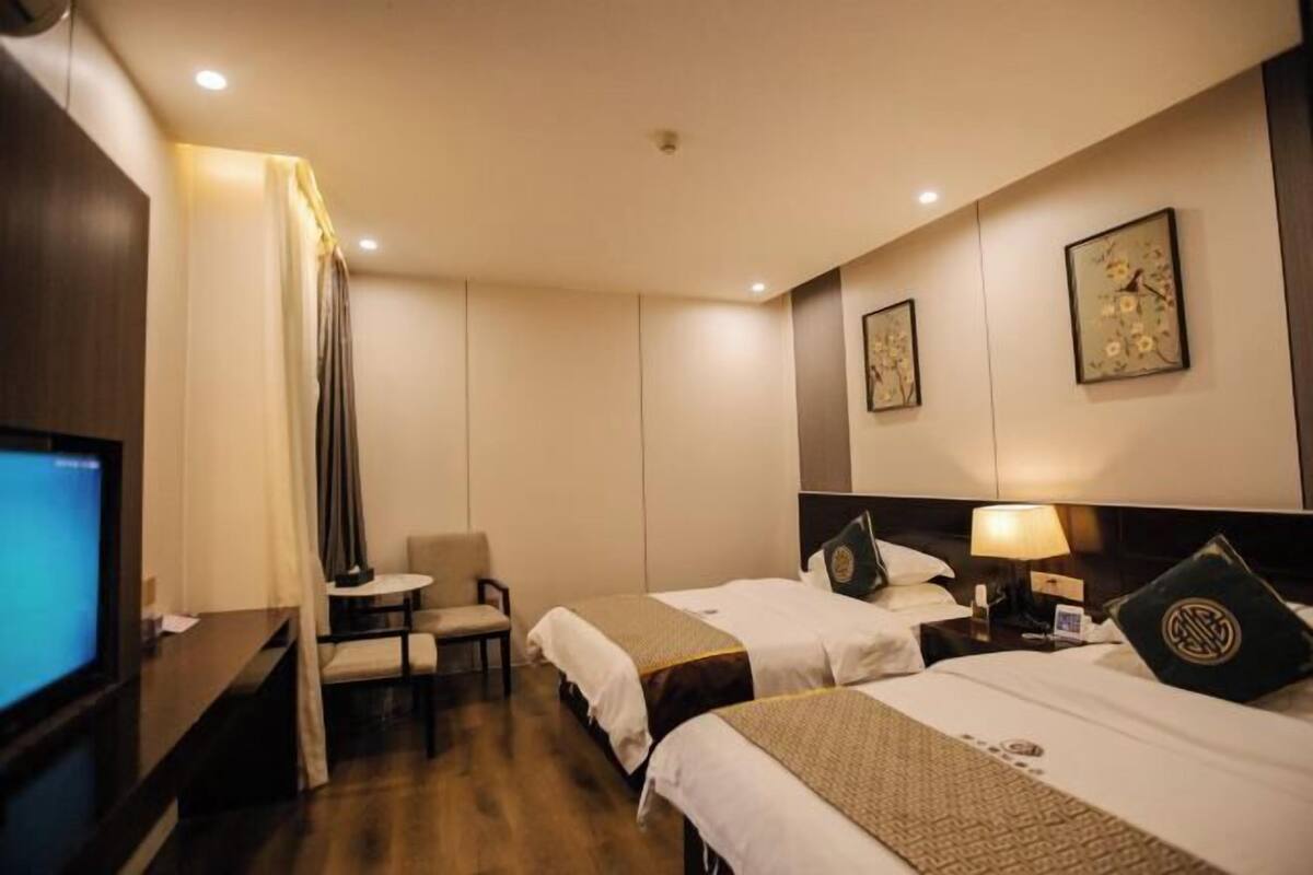 A hotel room with two beds, a desk with a computer, a chair, and a TV.