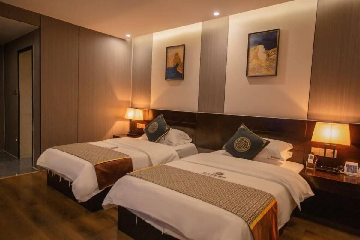 A hotel room with two beds, a wooden floor, a wall-mounted TV, and a door leading to another room.