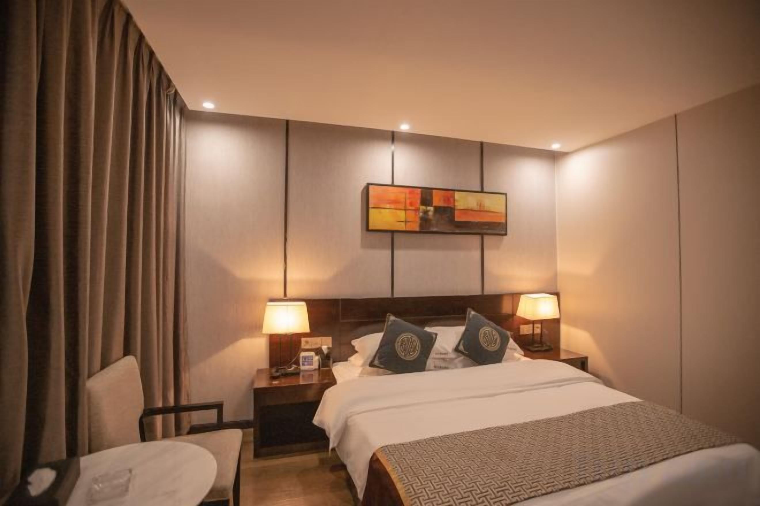 A hotel room with a bed, two bedside lamps, a nightstand, a chair, and a painting on the wall.