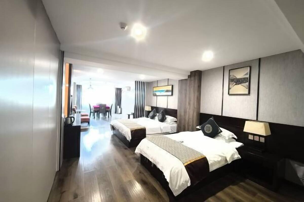 A hotel room with two beds, a dining area in the background, and a modern design with wooden flooring and neutral color palette.
