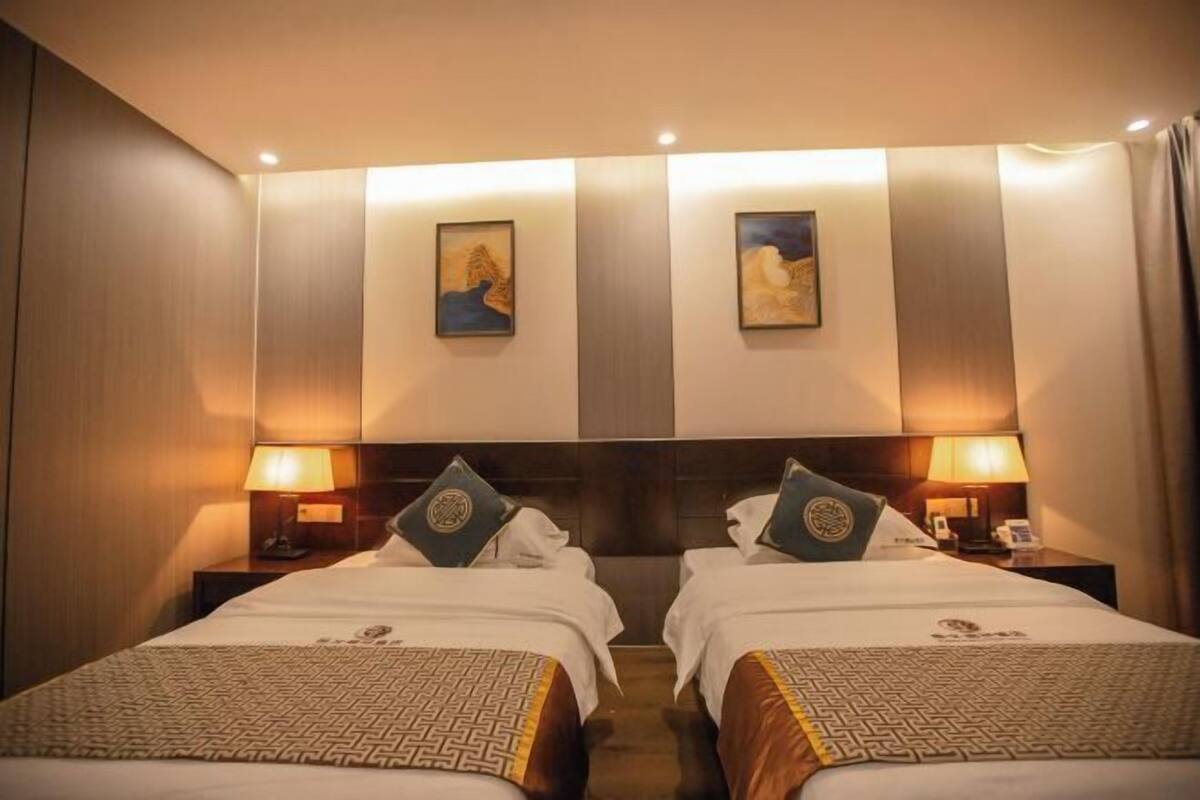 A hotel room with two beds, a headboard, bedside lamps, and artwork on the wall.