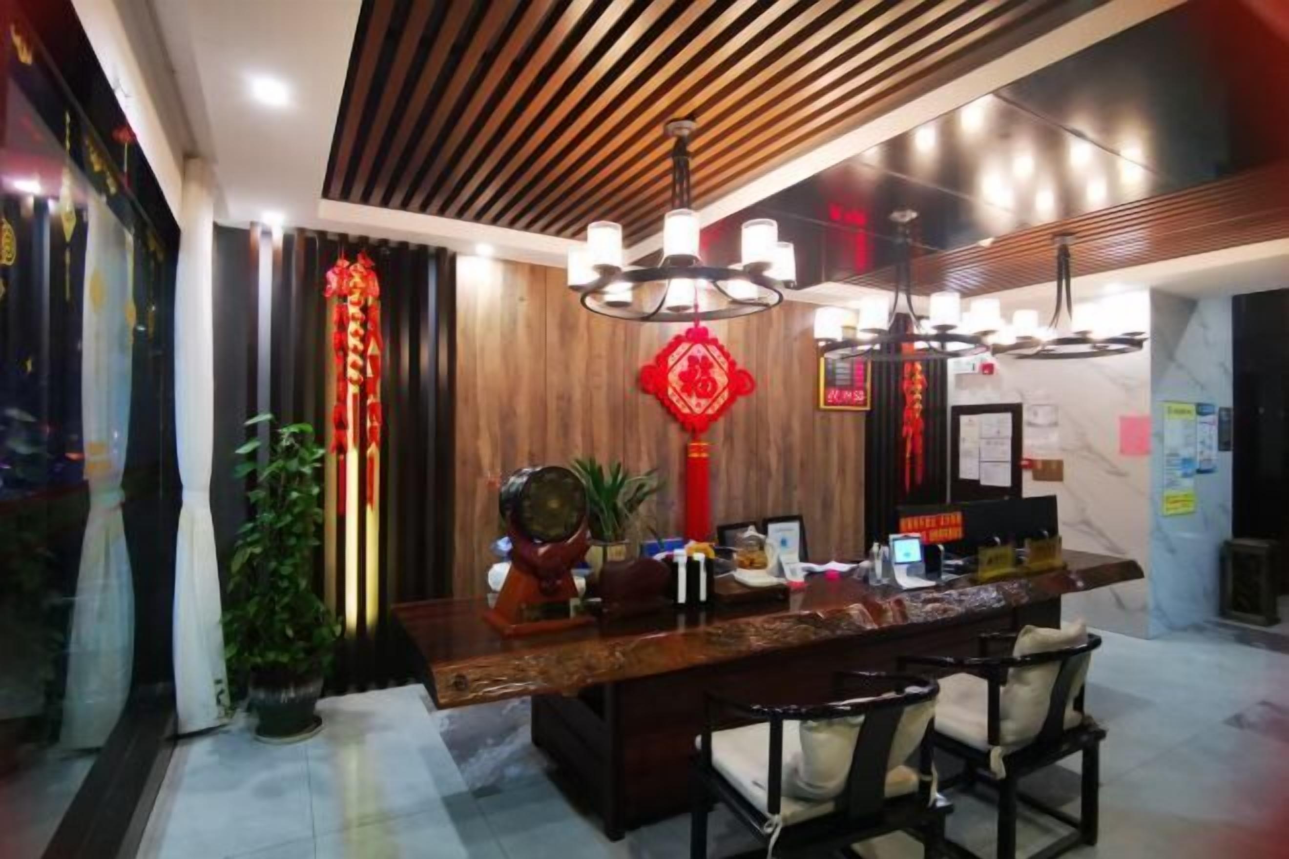 A reception area with a wooden reception desk, two chairs, a potted plant, and traditional red decorations.