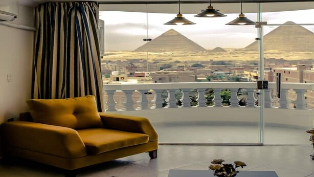 A room with a sofa, a view of the pyramids, and pendant lights. - Pyramids Bay Apartment the best place to view the Giza Pyramids (Giza Governorate)