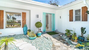 Un bâtiment blanc doté d’un patio carrelé, de plantes en pot et d’un petit arbre.