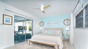 Une chambre à coucher avec un lit, un ventilateur de plafond, une grande fenêtre et une vue sur l’extérieur.
