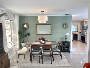 Un comedor con una mesa y sillas de madera, una lámpara colgante y una cocina al fondo.