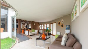 A modern living room with a glass door leading to a balcony, a sofa, a coffee table, and a dining area with a staircase. - Harmonie Hotel de Montaña (Villa General Belgrano)