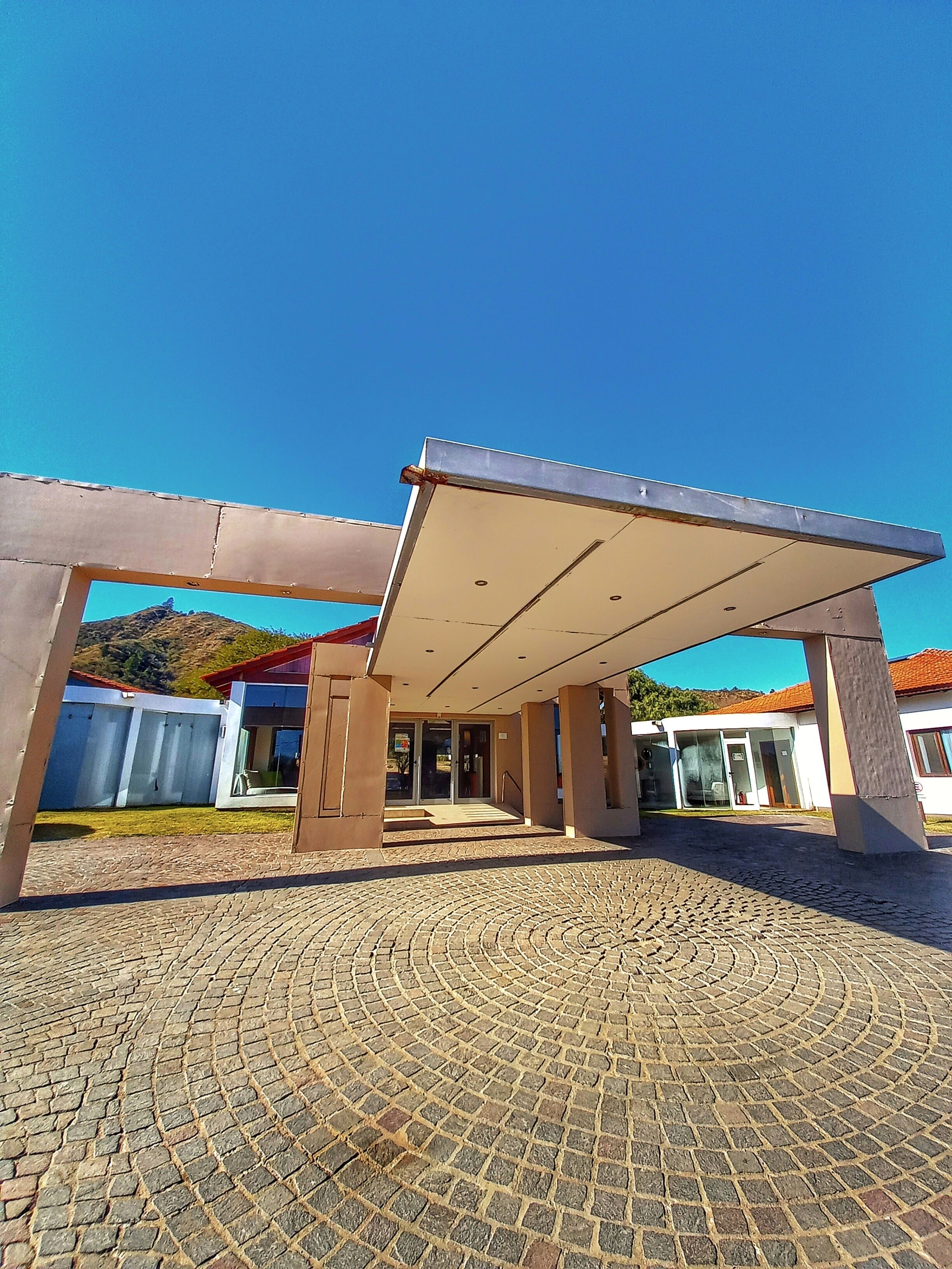 A building with a covered entrance, a paved courtyard, and a mountain in the background.
