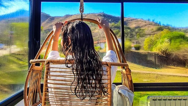 A person relaxing in a wicker chair by a large window overlooking a scenic landscape. - Harmonie Hotel de Montaña (Villa General Belgrano)