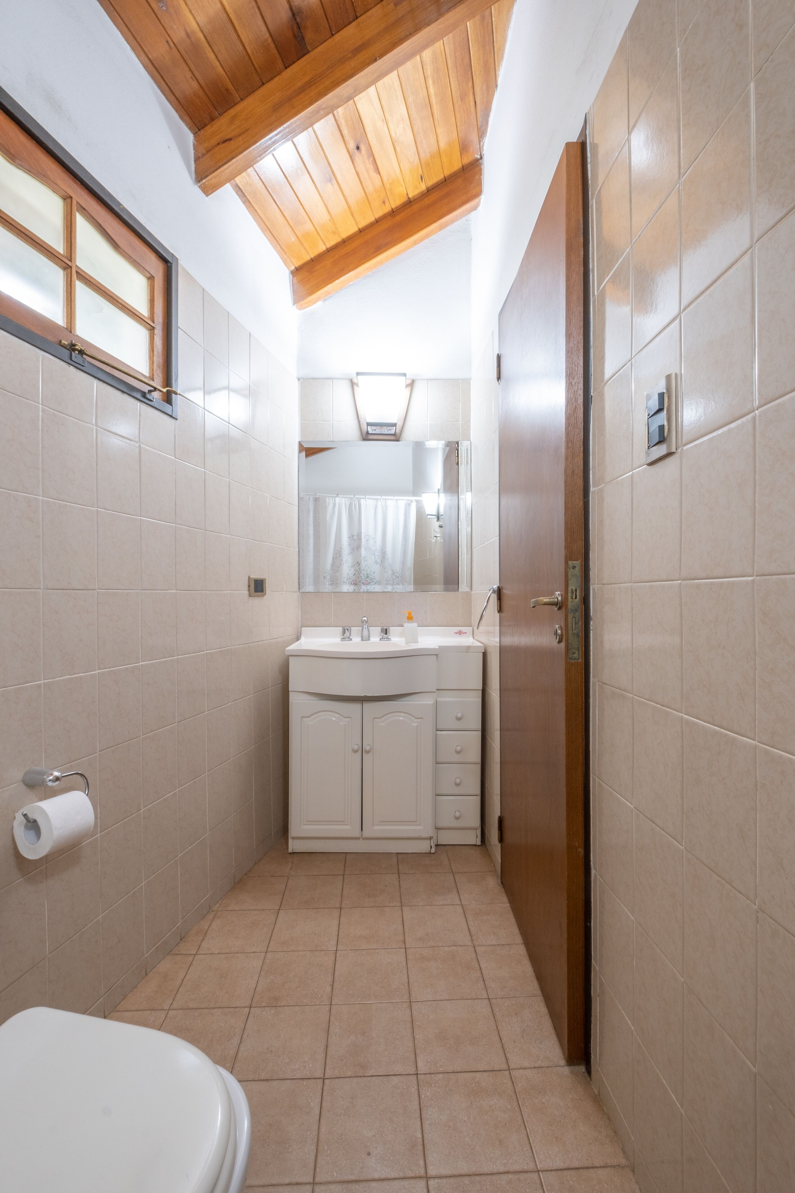 A compact bathroom with a wooden ceiling, a toilet, a sink with a mirror, and a cabinet.