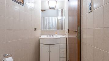 A compact bathroom with a wooden ceiling, a toilet, a sink with a mirror, and a cabinet.