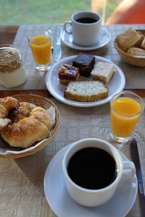 A breakfast table with croissants, a plate of pastries, a glass of orange juice, and a cup of coffee.