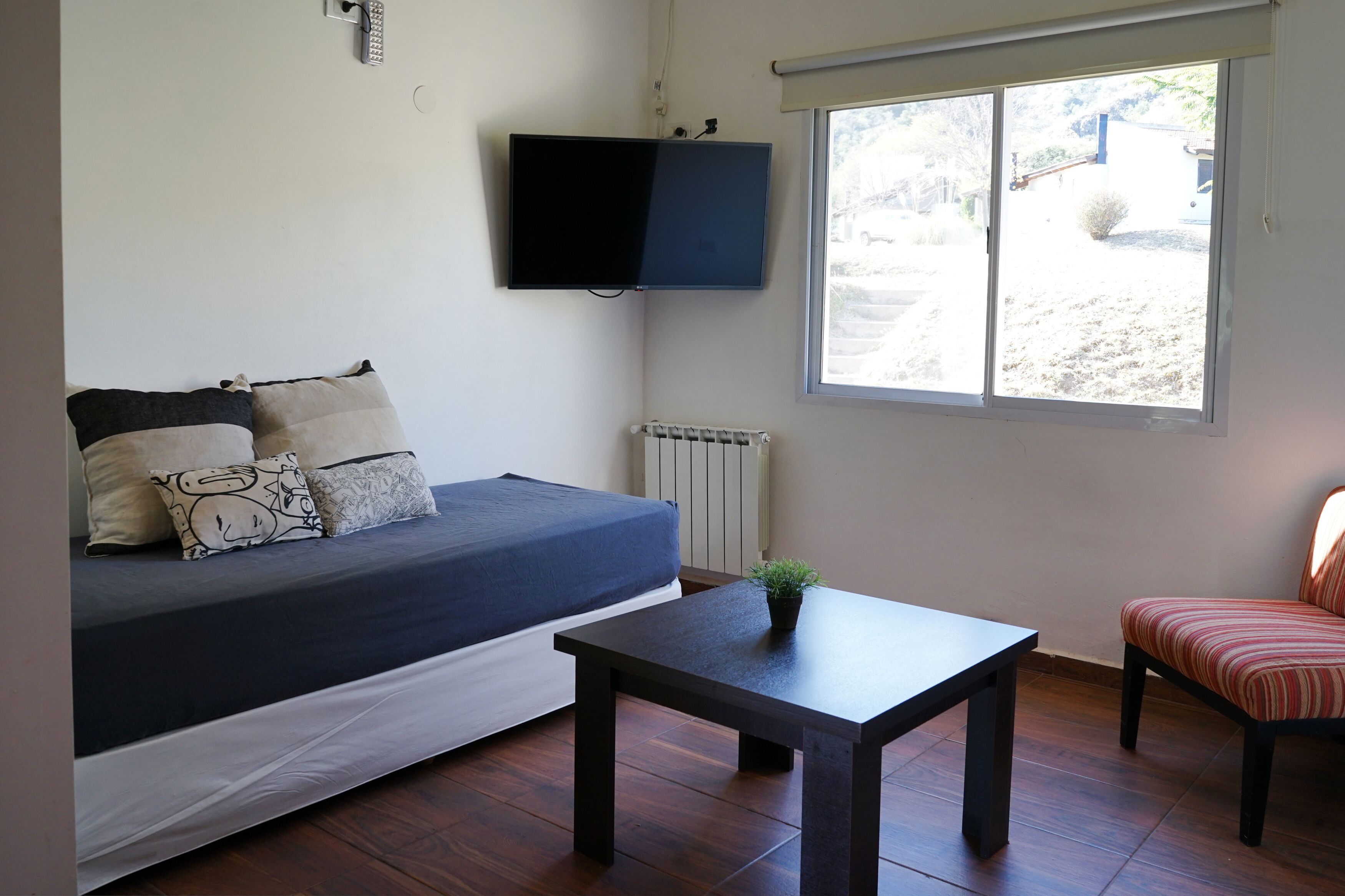 A room with a bed, a table, a chair, a TV, and a window.