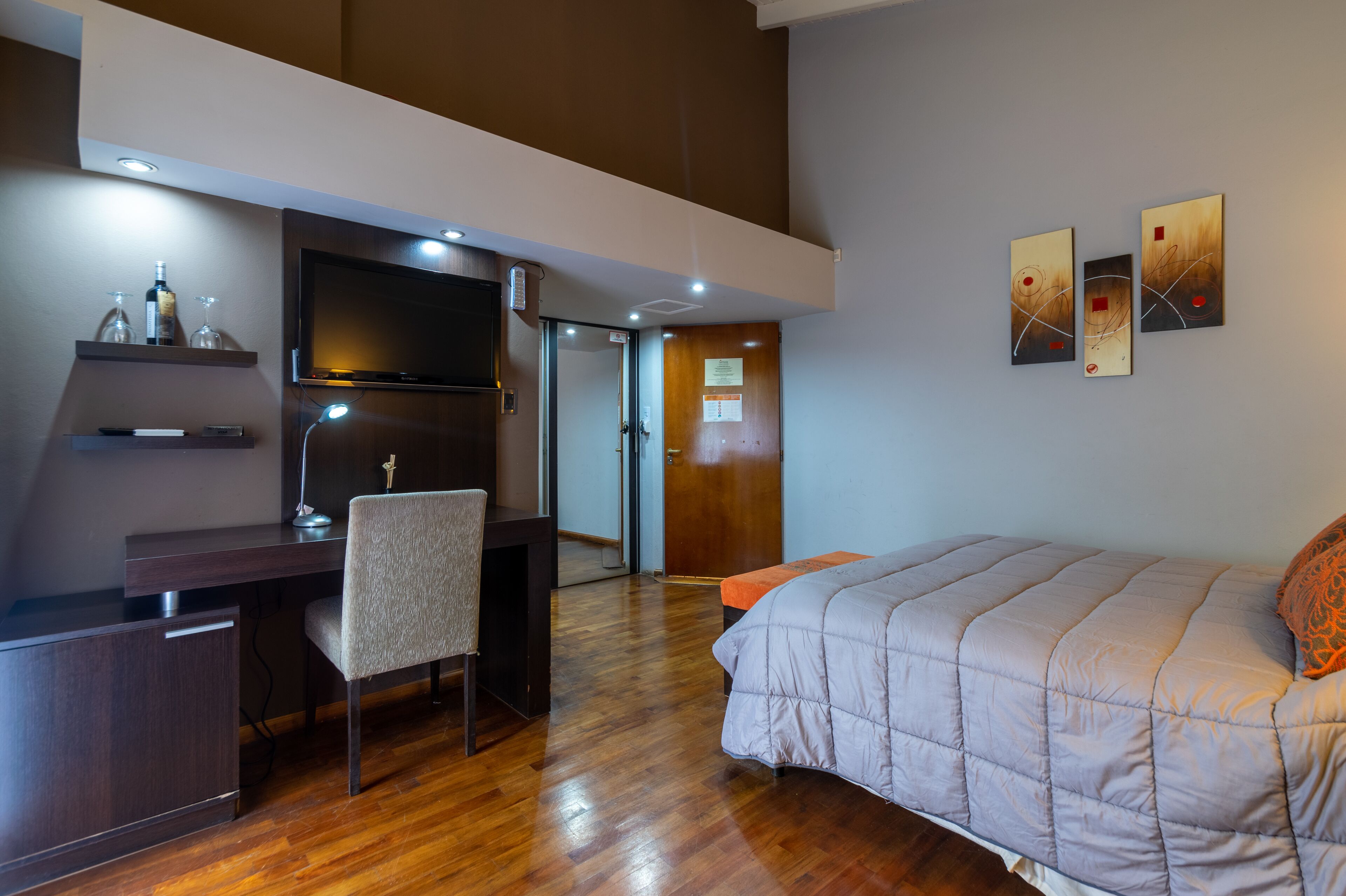 A modern hotel room with a wooden desk, chair, and bed.