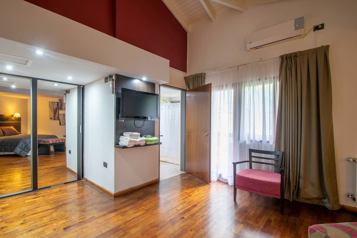 Une chambre d’hôtel avec un plancher en bois, un lit, une télévision, un bureau avec une chaise et une fenêtre avec des rideaux.