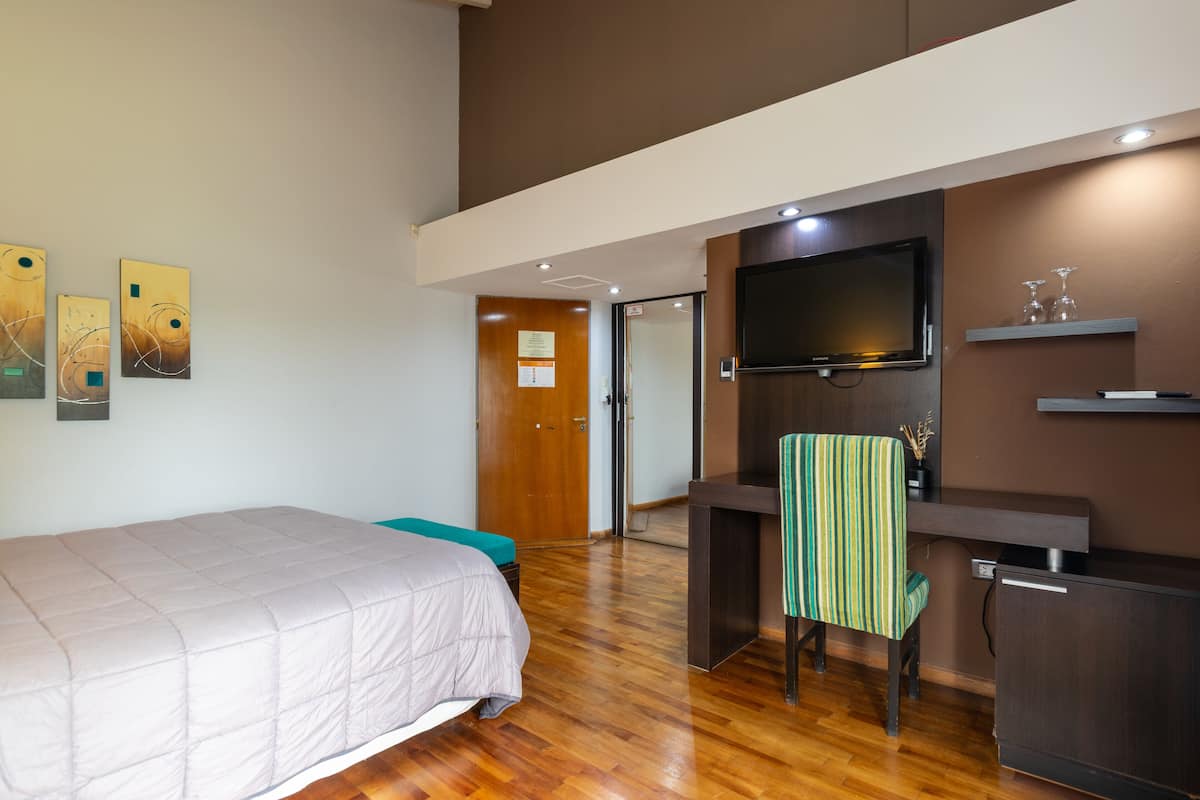 Une chambre d’hôtel avec un lit, un bureau, une chaise, une télévision et des œuvres d’art accrochées au mur.