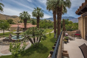 Relax in a serene garden setting with a central fountain, surrounded by palm trees and a mountainous backdrop.