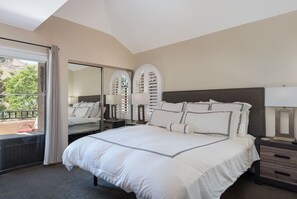 A bedroom with a large bed, a nightstand, a mirror, and a view of the outdoors.