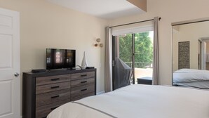 Un dormitorio con una cama, un televisor sobre una cómoda y un ventanal corredero que da a un espacio exterior.