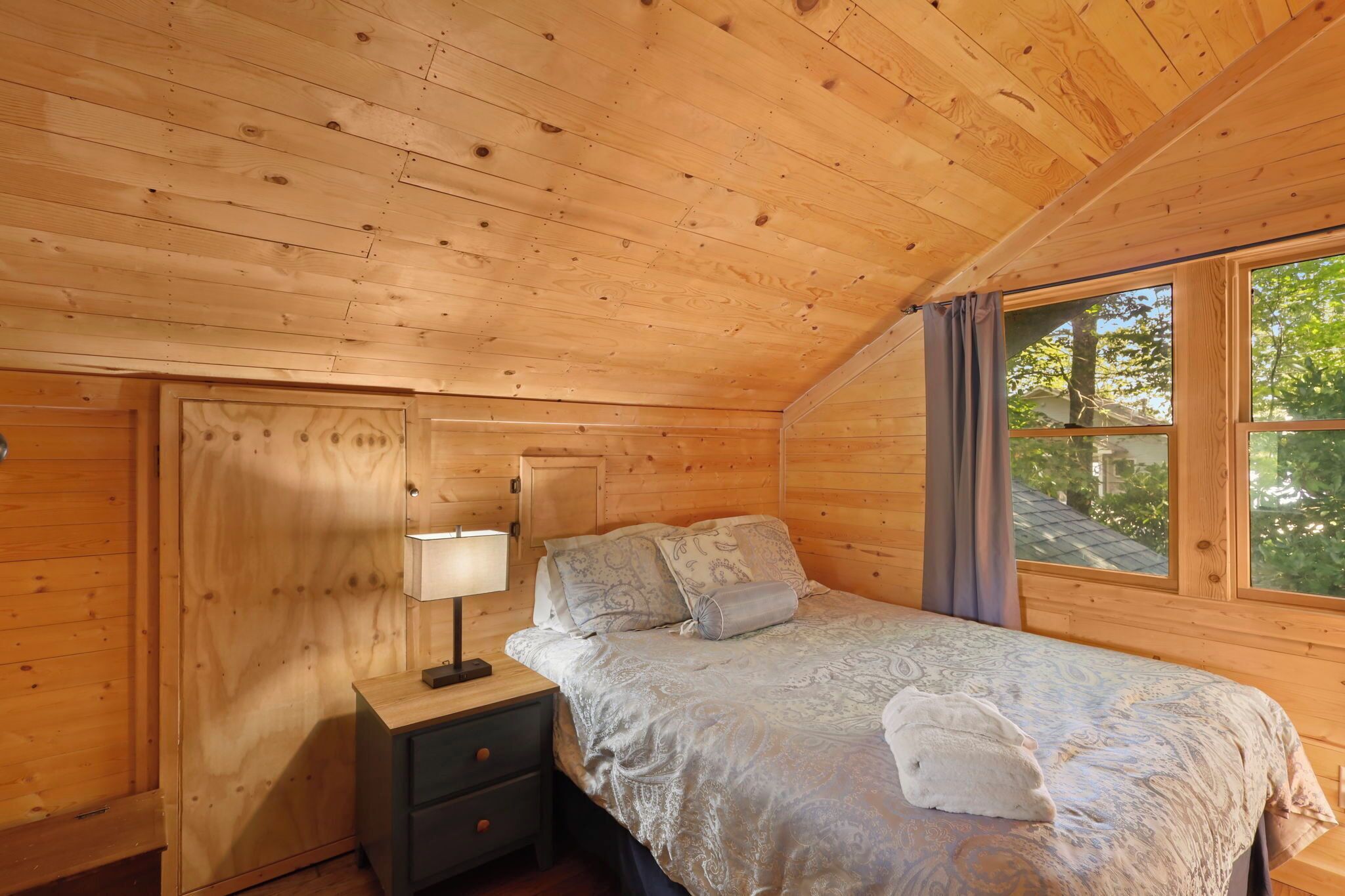 Un dormitorio de cabaña de madera con cama, mesita de noche y ventana.