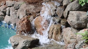 En pool med ett litet vattenfall som omges av stenar och ett trästaket.