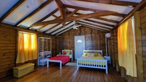 A cabin with a high ceiling, wooden beams, a bed, a bench, and a small table.
