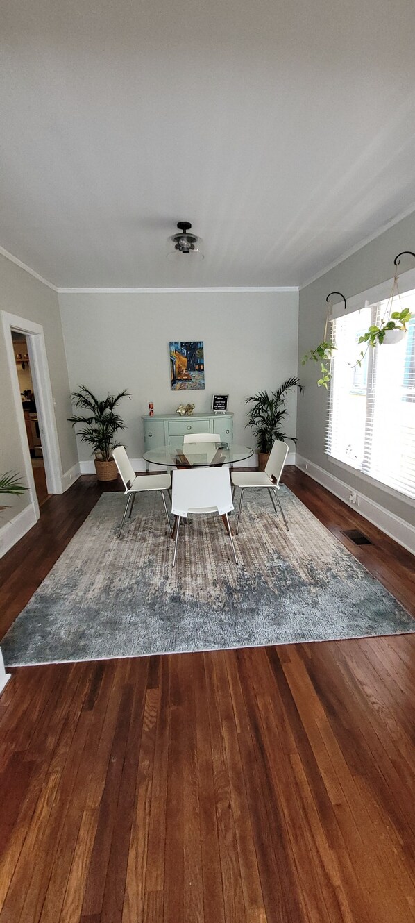 Uma sala de jantar com uma mesa redonda e quatro cadeiras, um ventilador de teto e uma janela grande com persianas.