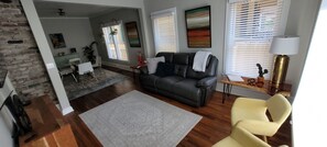 Uma sala de estar com sofá, uma poltrona amarela, luminária e um espaço de jantar com mesa e cadeiras.