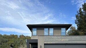 A modern two-story house with a garage, surrounded by natural vegetation. - Treetop Modern Oasis Lakeway (Austin)